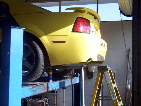 2002 Ford Mustang - A yellow 2002 Ford Mustang is raised on a hydraulic lift in a garage, showing its rear end.