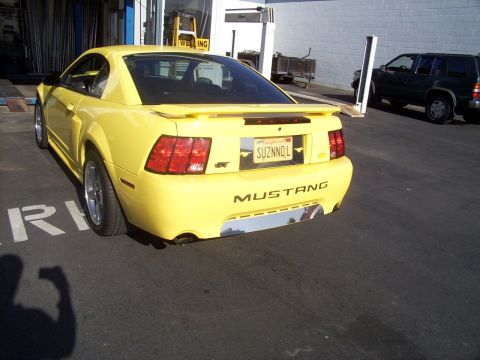 2002 Ford Mustang - A yellow 2002 Ford Mustang GT is parked in a lot, showing its rear end and a custom license plate.