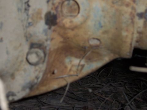 1983 Ford Bronco - Tight, slightly blurred close-up of the lower rear corner of a body panel or bedside, showing peeling white paint over faded blue and heavy…