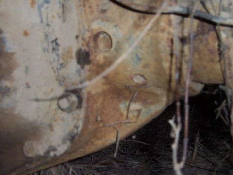 1983 Ford Bronco - Soft-focus close-up of a badly rusted lower body panel where white paint has flaked away to bare metal and older blue paint, with stamped d…