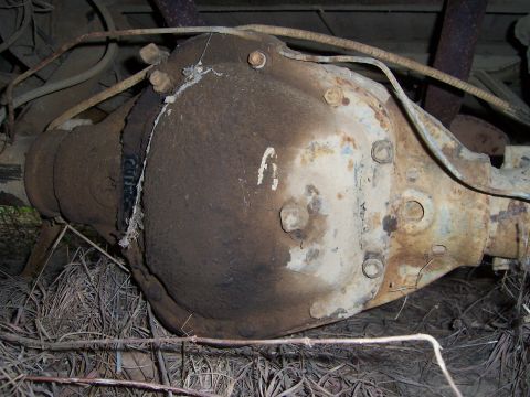 1983 Ford Bronco - Close-up underside view of a heavily rusted solid axle housing and its bolt-on differential cover, with flaking paint, dirt buildup and a t…