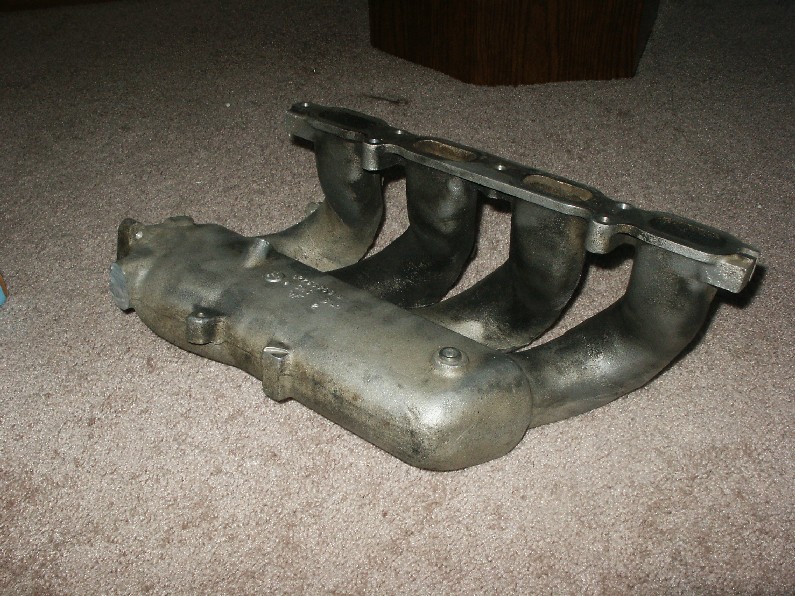 Cast metal intake manifold with four runners on beige carpet