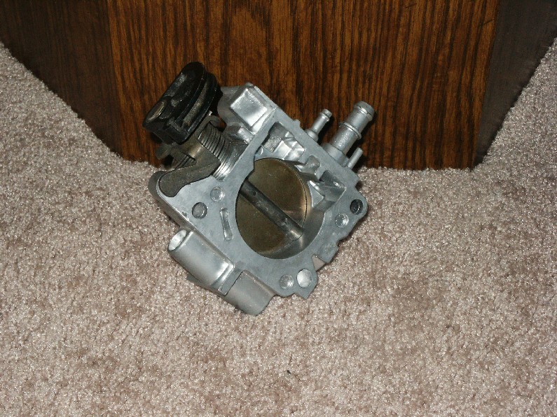 Aluminum throttle body with black sensor and coolant nipples on carpet