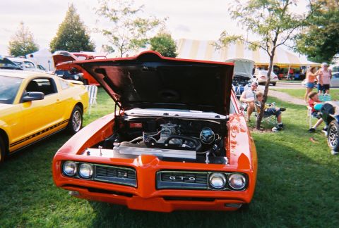 1996 Ford F-150 - A classic orange Pontiac GTO is displayed with its hood open at an outdoor car show.