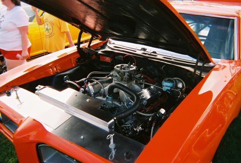 1996 Ford F-150 - The engine bay of an orange car is open, revealing a V8 engine and chrome components. Two people are visible in the background.