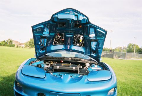 1996 Ford F-150 - The engine bay of a blue car is visible with the hood open, revealing custom painted details on the underside of the hood.