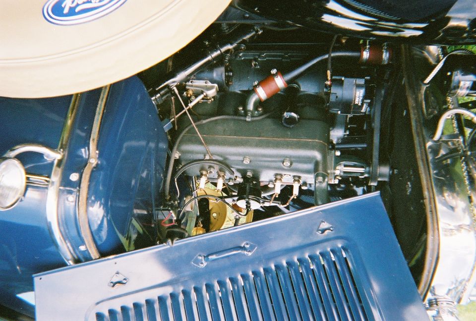 Close-up of a vintage car's engine bay, showing the engine, hoses, and part of the blue bodywork