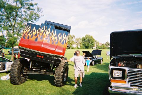 1996 Ford F-150 - A modified truck with flame decals and oversized tires is displayed at an outdoor event with other vehicles.