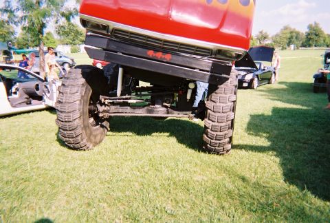 1996 Ford F-150 - A heavily modified pickup truck with oversized tires is displayed on a grassy field, with other vehicles visible.