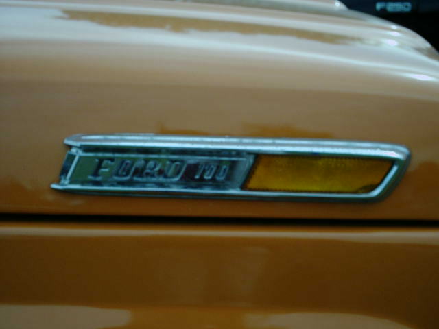 Chrome fender emblem reading FORD 100 with amber side reflector on orange bodywork