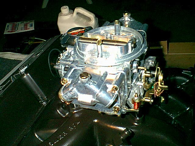 Polished aftermarket four-barrel carburetor sitting on an intake manifold in a workshop