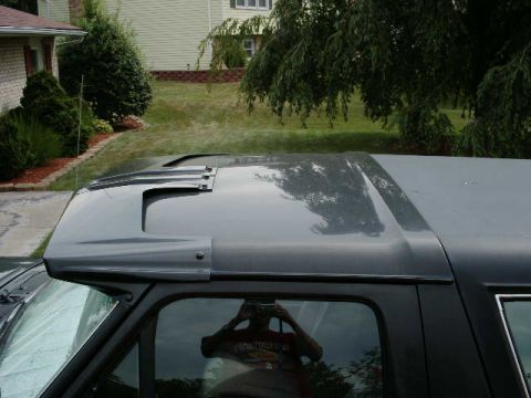 1992 Ford Bronco - The top of a dark-colored SUV is shown, an aftermarket sun visor. The photographer is reflected in the side window.