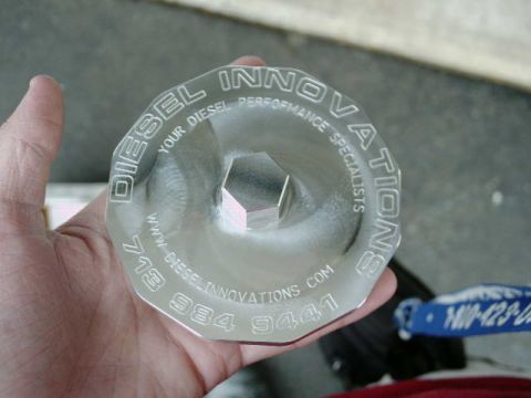 2002 Ford F-250 - A hand holds a metal cap with 'DIESEL INNOVATIONS YOUR DIESEL PERFORMANCE SPECIALISTS' engraved on it.