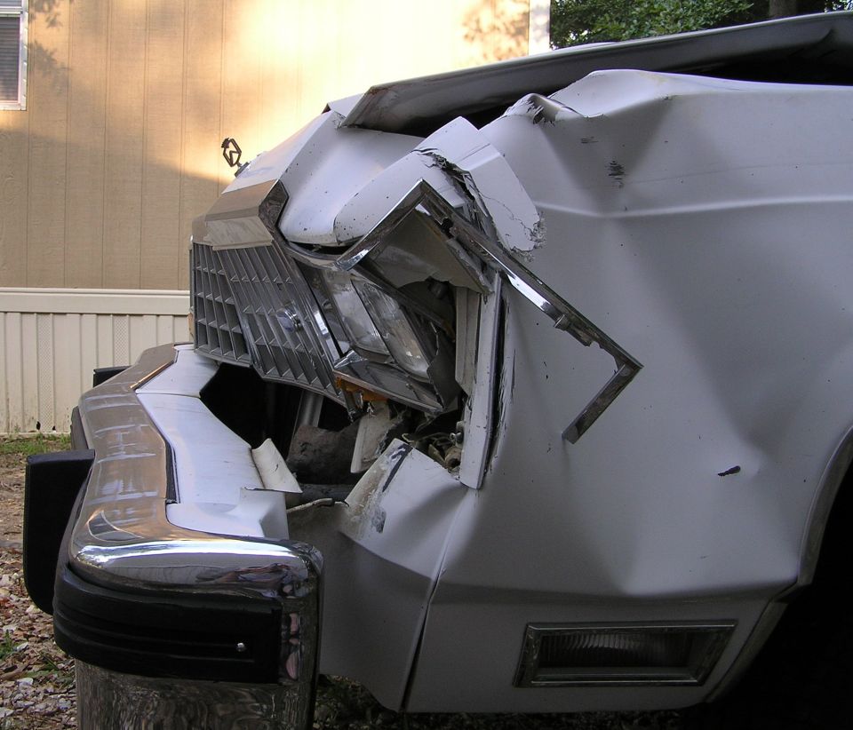 Close-up of severe front-corner crash damage on a white car, headlight and fender torn apart