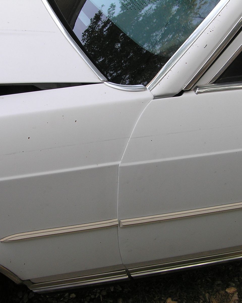 Close-up of a creased and dented white car door and rear quarter panel with chrome trim