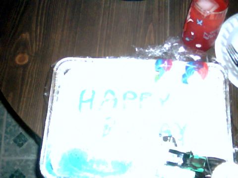 1992 Ford Bronco - A cake with 'HAPPY' written on it sits on a wooden table next to a red drink.