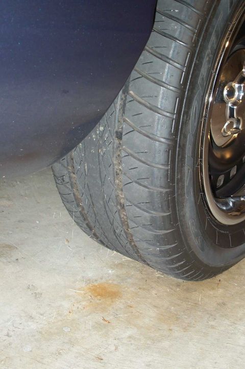1998 Ford Crown Victoria - Close-up of a worn tire and wheel on a dark-colored vehicle.
