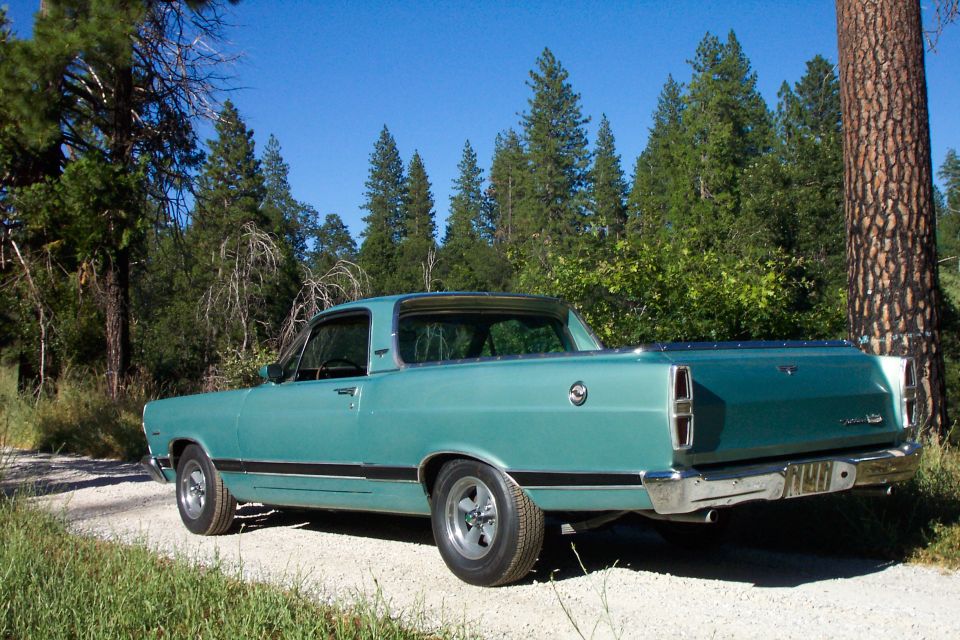 Teal 1967 Ford Ranchero, rear three-quarter view, parked on gravel road among pine trees
