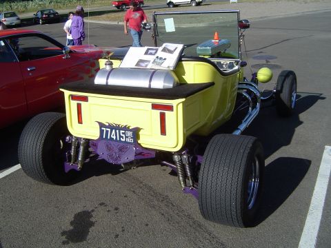 1964 Ford Fairlane - A yellow hot rod with a custom license plate frame is parked next to a red car.