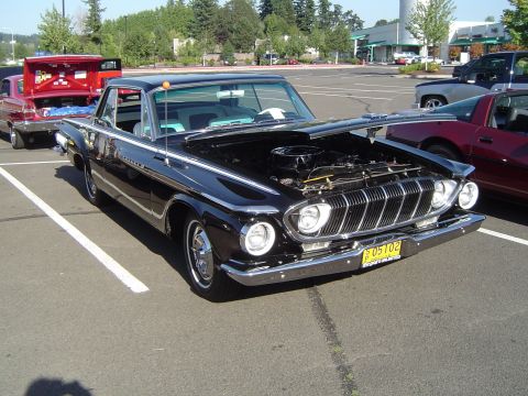 1964 Ford Fairlane - A black 1961 Dodge Polara is parked with its hood open, revealing the engine and front grille. Another vehicle is visible in the background.