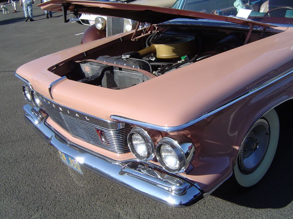 Front view of a pink 1960 Imperial with hood open, showing engine. Chrome grille and headlights visible