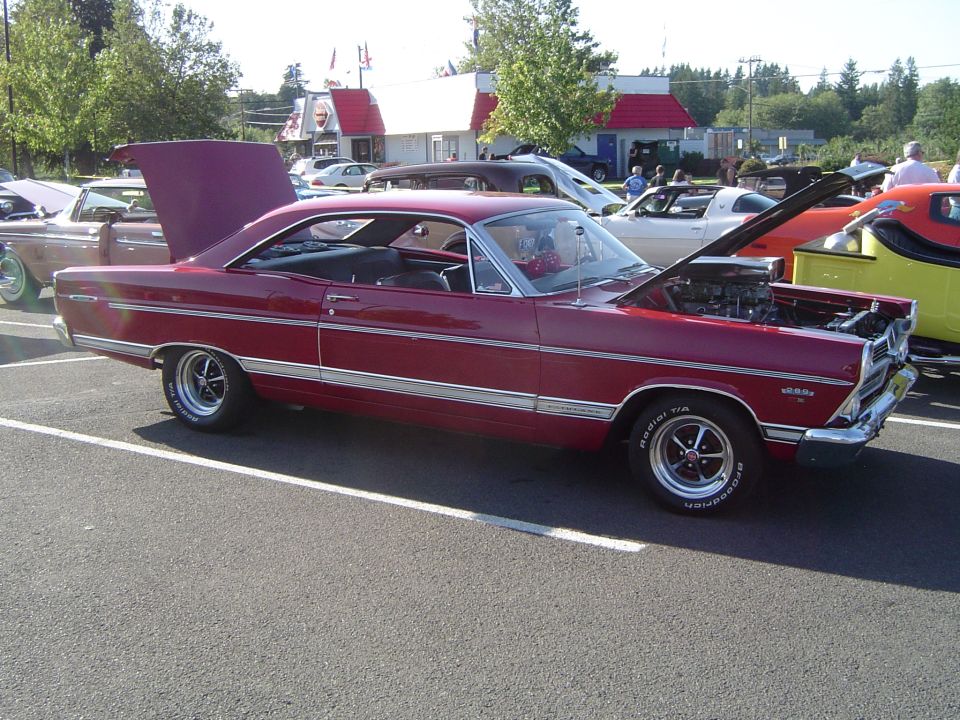 Red coupe with hood and trunk open, parked in a lot. Chrome trim and racing wheels are visible