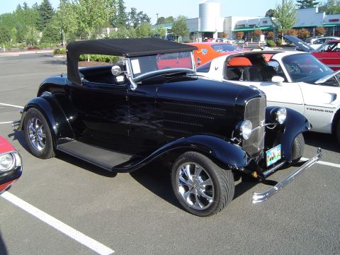 1964 Ford Fairlane - A black convertible hot rod with flame decals and chrome wheels is parked in a lot next to other vehicles.