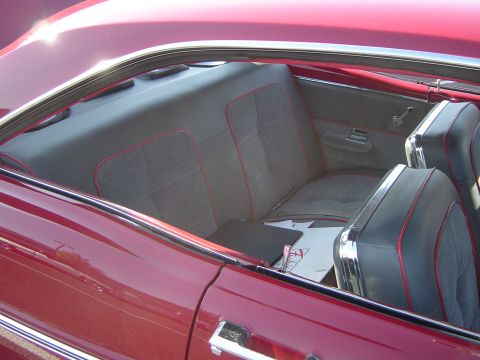 1964 Ford Fairlane - Close-up of the interior of a red vehicle, showing the rear seating area and door panel details.