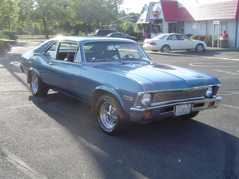 1964 Ford Fairlane - A blue 1970 Chevrolet Nova coupe is parked in a lot, with a white sedan visible in the background.
