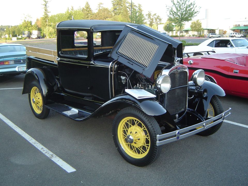 Black pickup truck with yellow wire wheels and hood open, parked next to a red car