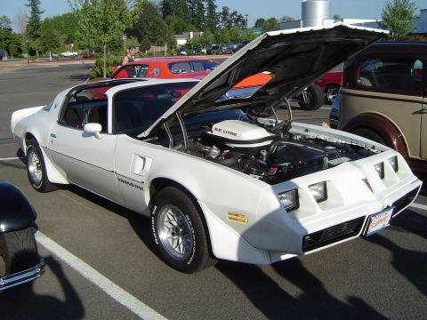 1964 Ford Fairlane - A white 1977 Pontiac Trans Am is parked with its hood open, revealing the engine.