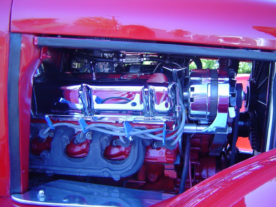 Engine bay showing chrome valve covers, red engine block, and alternator