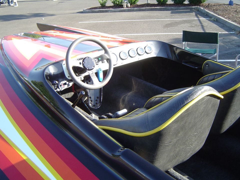 Interior of a speed boat with rainbow stripes on the hull, showing the steering wheel, dashboard gauges, and bucket seats