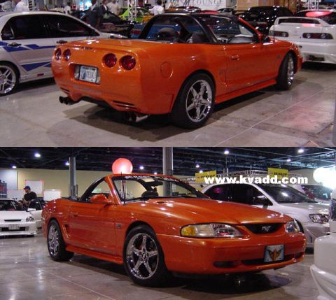 2000 Ford Crown Victoria - Two orange convertible sports cars are displayed indoors at an event.