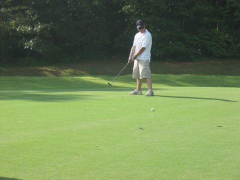 1976 Ford Maverick - A man putts a golf ball on a green with trees in the background.