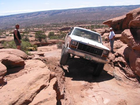1981 Ford Bronco - A white off-road SUV navigates a challenging rocky terrain with two people observing.