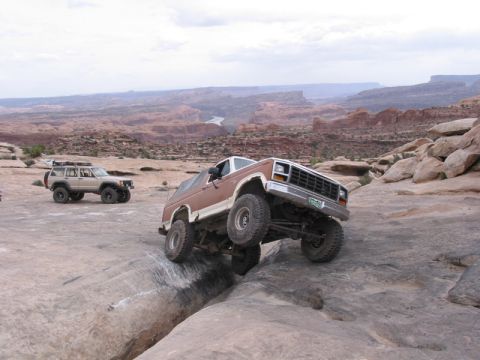 1981 Ford Bronco - Two off-road vehicles navigate a rocky trail in a desert landscape.