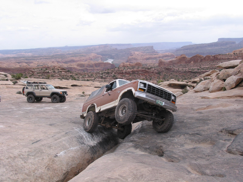 Brown Ford Bronco climbing over rocks with another SUV in the background