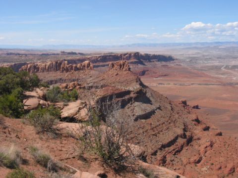 1981 Ford Bronco - A vast desert landscape unfolds with layered rock formations and distant mesas under a bright, partly cloudy sky.