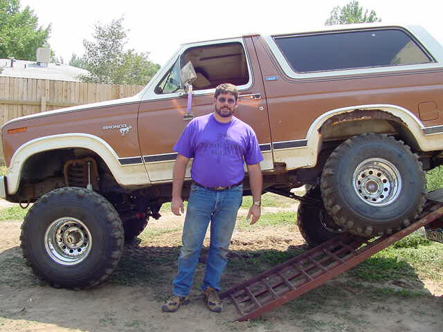 1981 Ford Bronco with large tires and a man standing on a ramp beside it