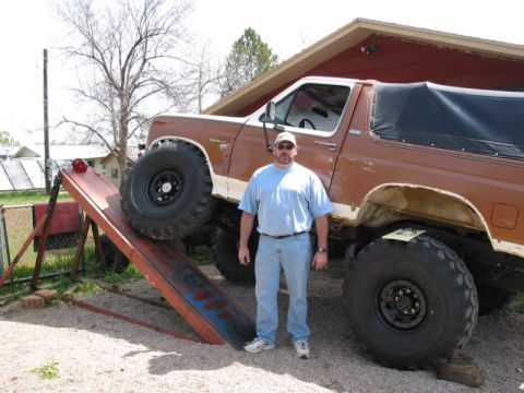 1981 Ford Bronco - A man stands next to a modified Ford Bronco with large off-road tires.