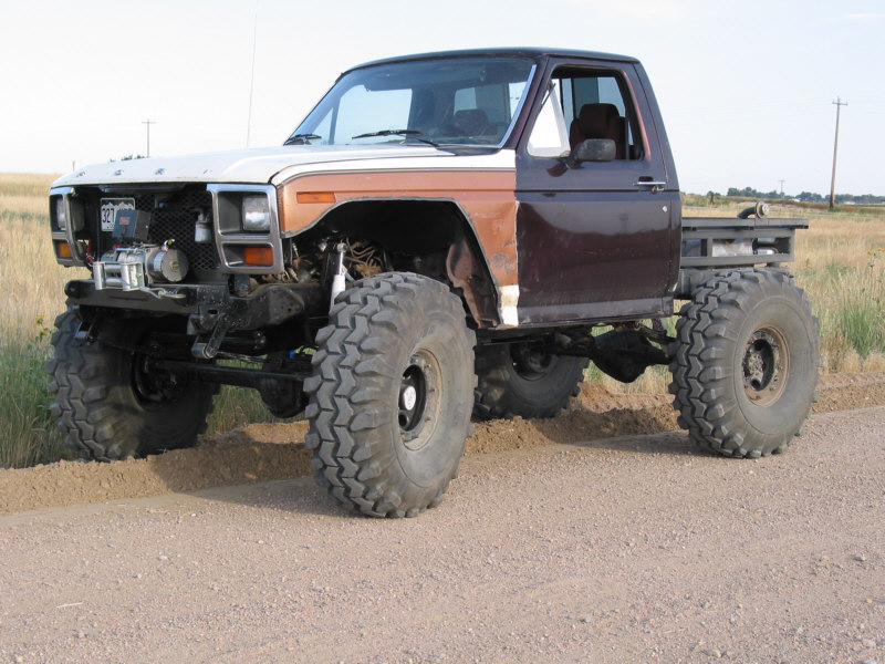 Hoodless two-tone lifted Ford flatbed 4x4 with winch bumper on gravel roadside