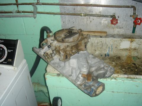 1986 Ford Mustang - A disassembled engine part, likely an intake manifold and carburetor, is shown in a utility area.