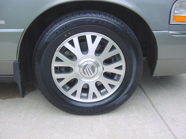 Mercury silver alloy wheel with center cap and Firestone tire on light green sedan