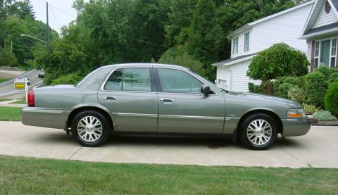 2003 Mercury Grand Marquis - A gray 2003 Mercury Grand Marquis sedan is parked on a concrete driveway in front of a house.