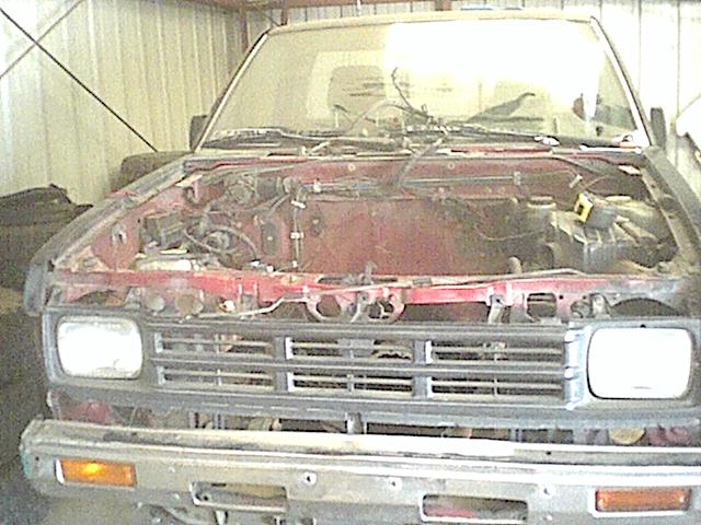 Red Nissan with hood removed and engine pulled, empty engine bay, parked in a garage