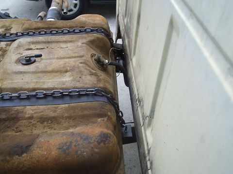 1979 Ford F-150 - A heavily rusted fuel tank is chained to the exterior of a white truck.
