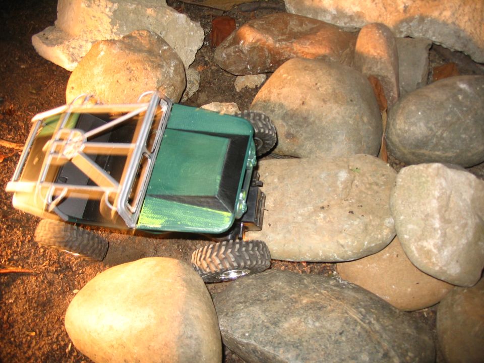 Green RC crawler climbing over rounded river rocks viewed from above