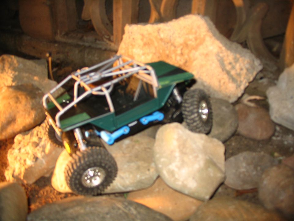 Green RC crawler with chrome roll cage and blue suspension links flexing over rocks