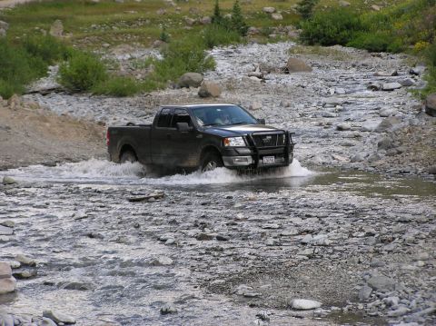 1986 Ford Bronco - This truck is navigating a shallow riverbed in a rocky, mountainous area.